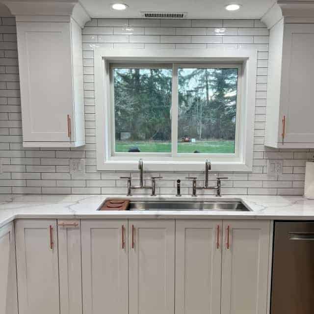 Full View of Kitchen Sink, two faucets. Window with view of a yard.